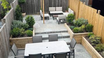 Un patio con una pérgola, mobiliario exterior y jardineras elevadas.