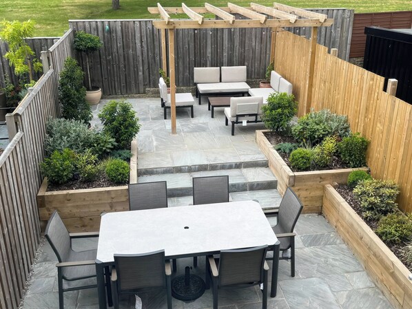 Une terrasse dotée d’une pergola, d’un espace salon extérieur et de jardinières surélevées.