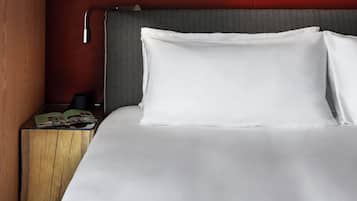 A neatly made bed with white linens, a headboard with a herringbone pattern, and a nightstand with a magazine and a black object.