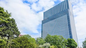 A modern high-rise building with a glass facade, surrounded by lush green trees.