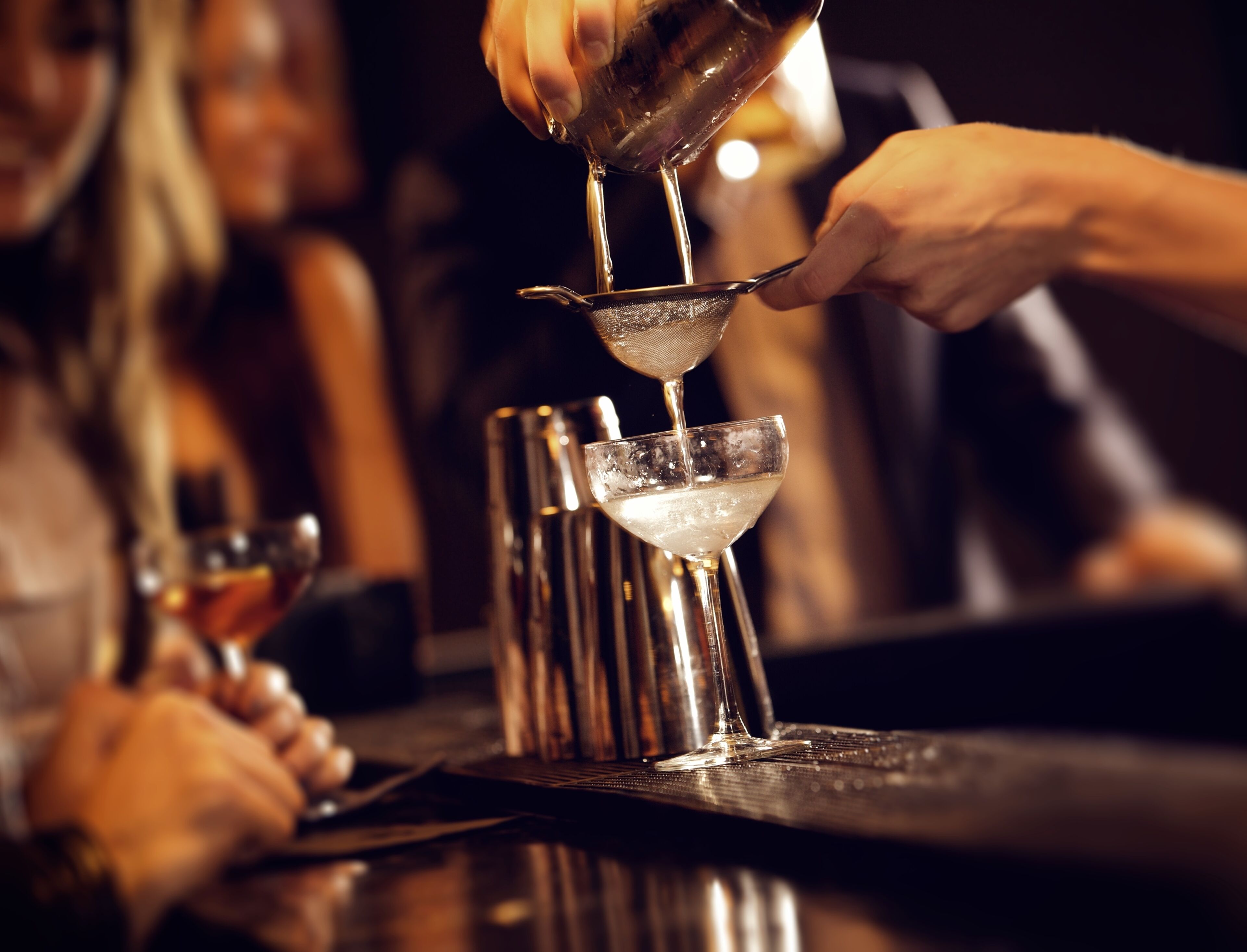 A bartender pouring a drink into a martini glass.