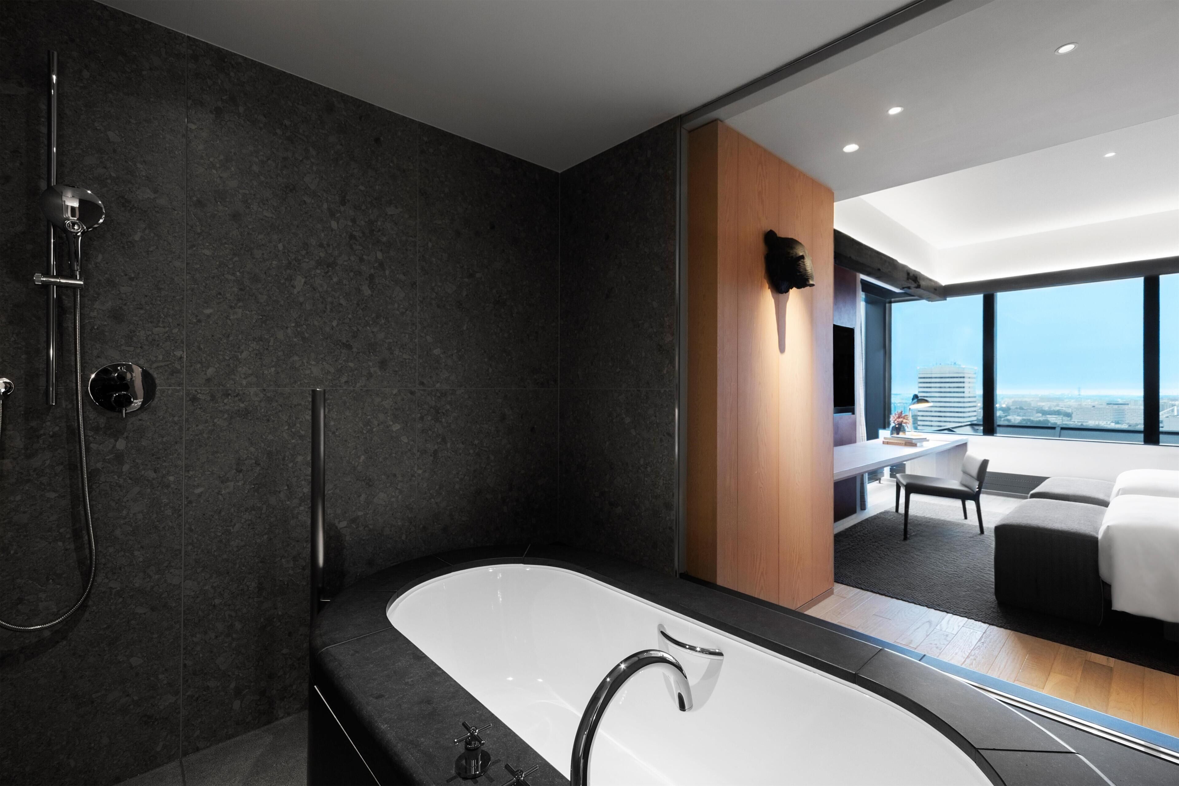 A modern bathroom with a large bathtub, a shower, and a view of a cityscape through large windows.