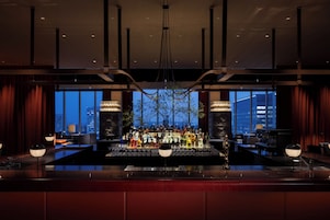 A bar area with a city view, large windows, and a variety of bottles.