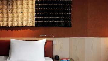 A neatly made bed with a white pillow, a bedside table with a lamp, and a small stack of books.