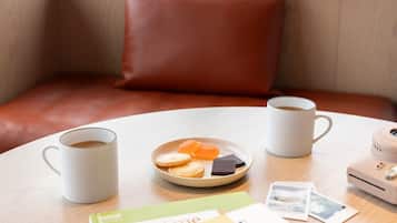 A cozy seating area with a round table, two white mugs, a plate with cookies and chocolate, a book titled 'blend me,' and a portable heater.