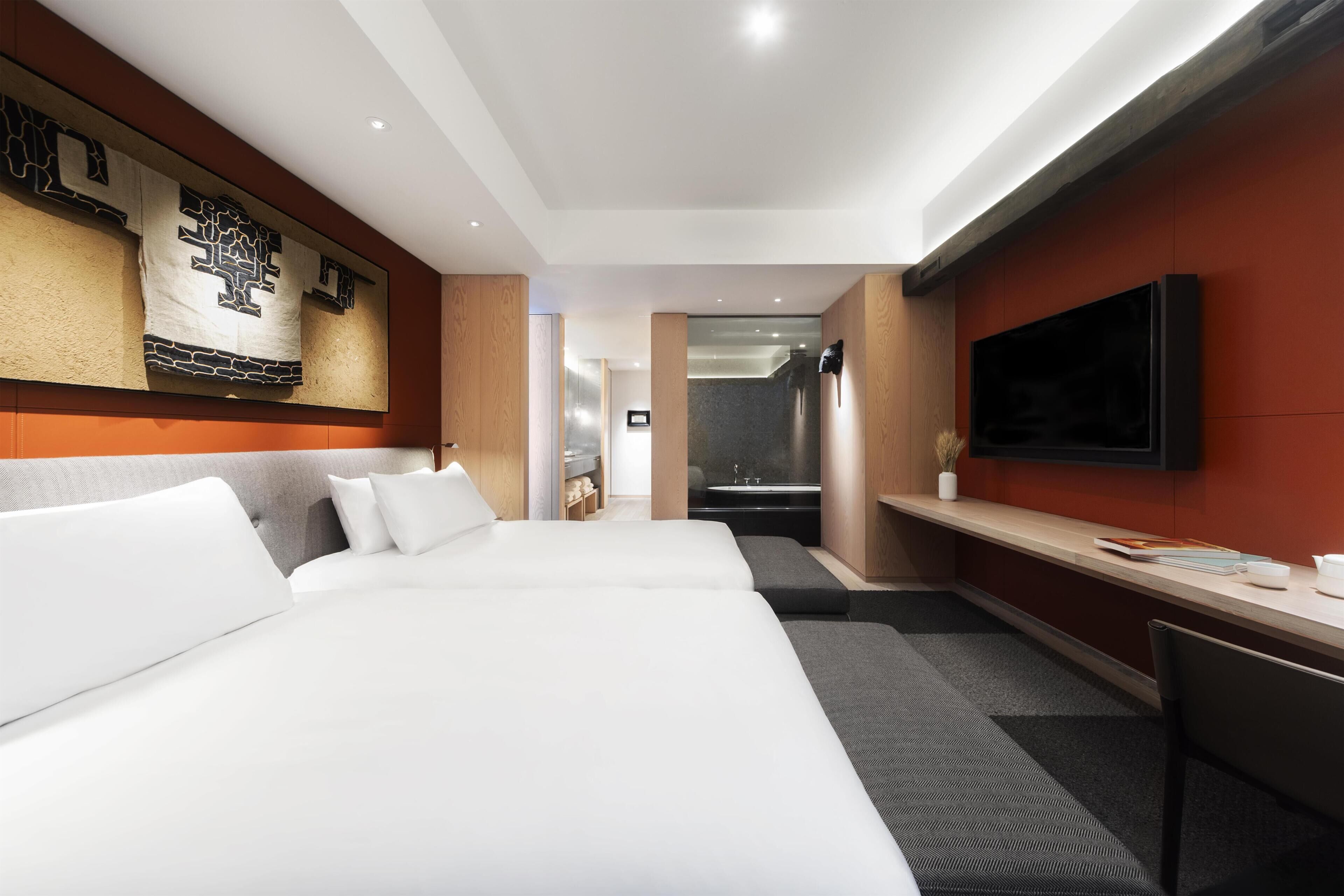 A hotel room with a large bed, a desk, a TV, and a bathroom visible through an open door.