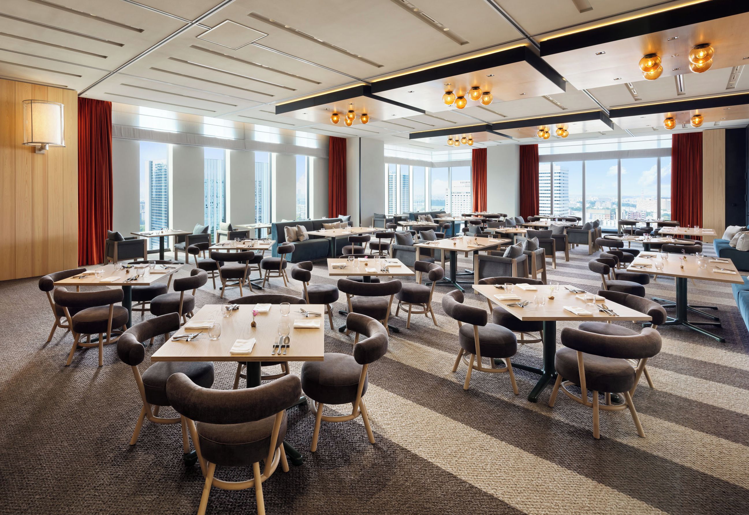 Une salle de conférence spacieuse, dotée de nombreuses tables et chaises, de grandes fenêtres offrant une vue sur la ville et d’un éclairage moderne.