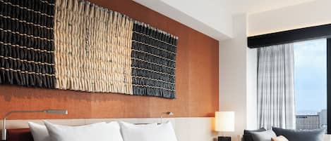 Habitación de hotel con una cama grande, una mesita de noche, una lámpara y vistas a la ciudad a través del ventanal.