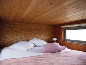 Une chambre avec un plafond en bois, un lit avec une literie blanche et rose, et une fenêtre donnant sur un beau paysage.