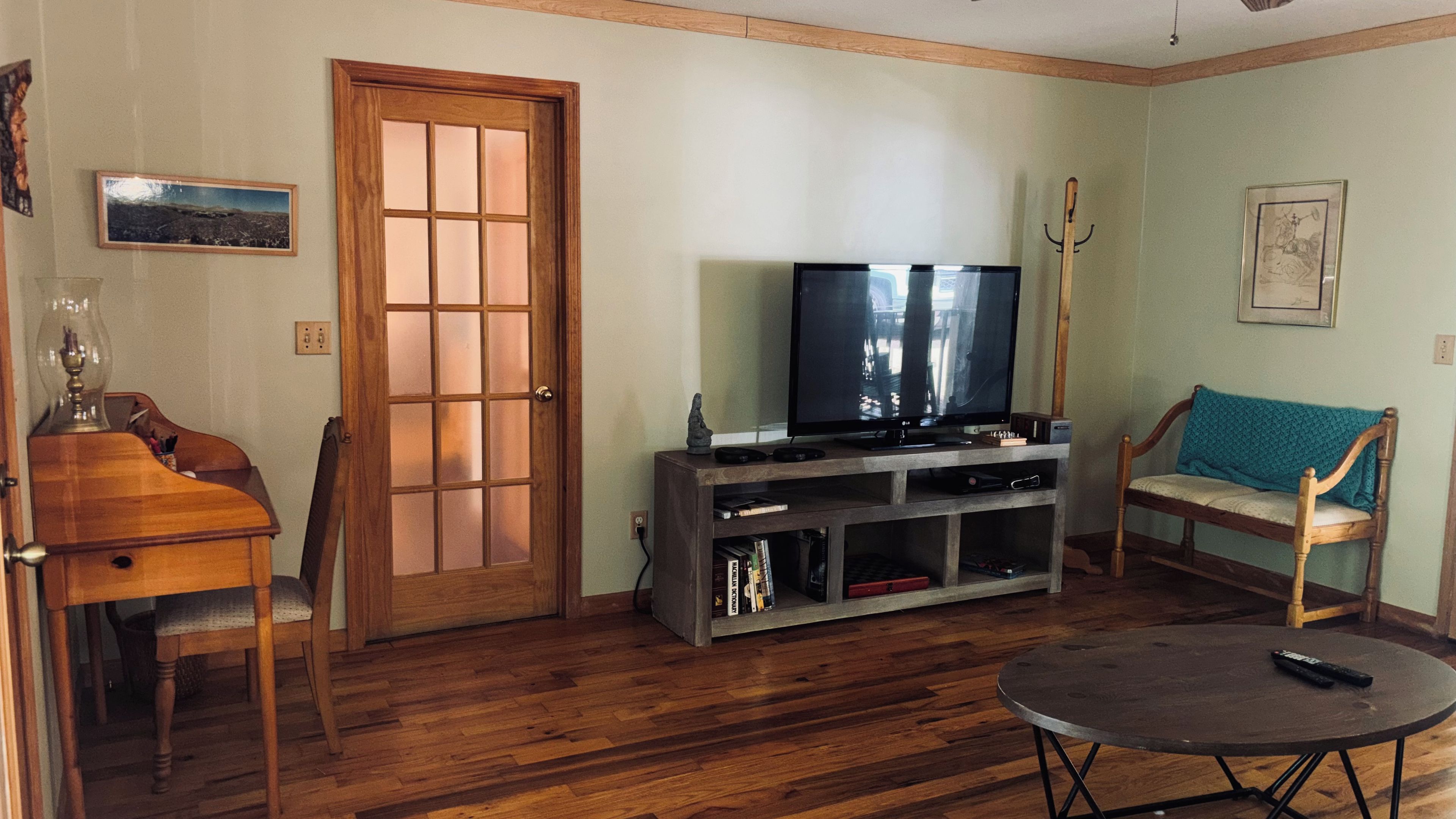 A living room with a wooden floor, a television on a stand, a sofa, a coffee table, and a door with glass panels.