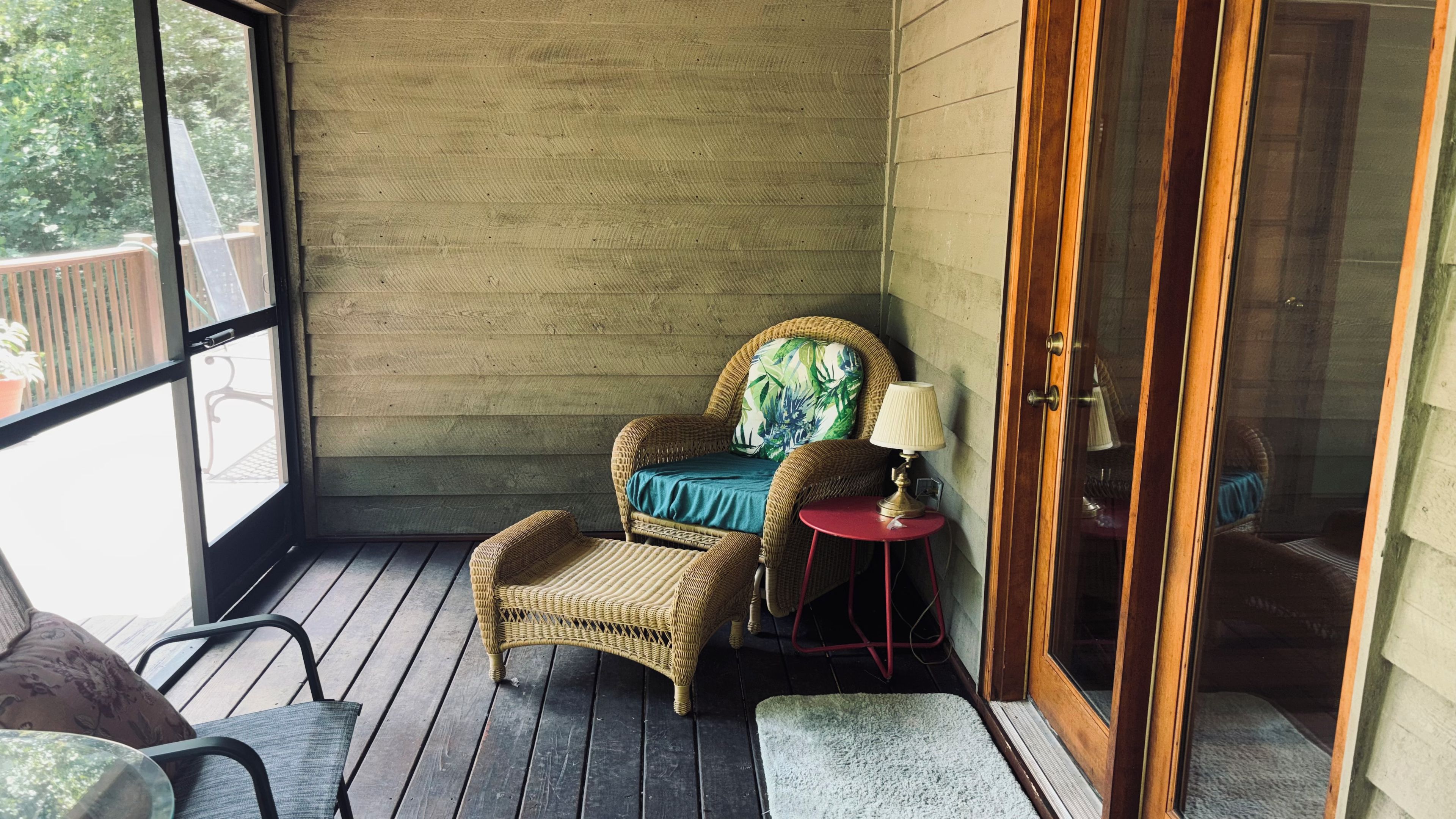 Una silla de mimbre con un cojín y una mesita con una lámpara sobre una terraza de madera.