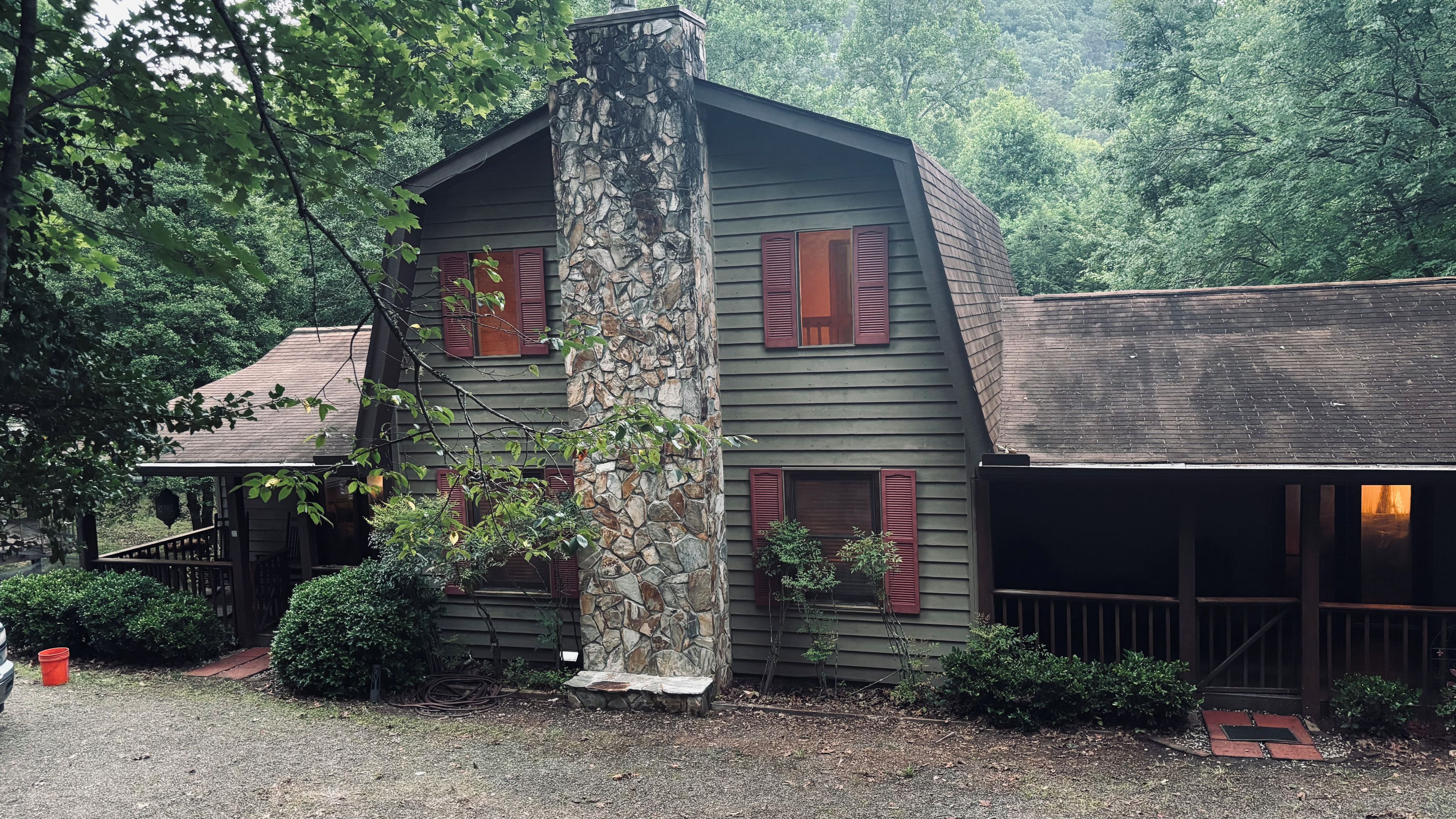 Une cabane rustique avec une cheminée en pierre, un revêtement en bois et des volets rouges.