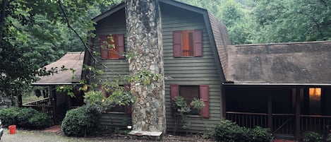 Une cabane rustique avec une cheminée en pierre, un revêtement en bois et des volets rouges.