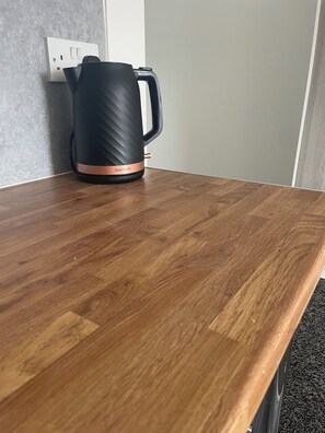 Une bouilloire noire avec une bande de cuivre, posée sur une table en bois.