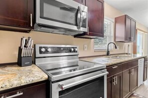 A kitchen with stainless steel appliances, dark wooden cabinets, and a granite countertop. - Villa Varges - Be our Guest! (Lehigh Acres)