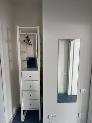 A narrow room with a white wardrobe, a mirror, and a small shelf with a box and hangers. - Bright Studio Apartment with Parking 205 (Milano)