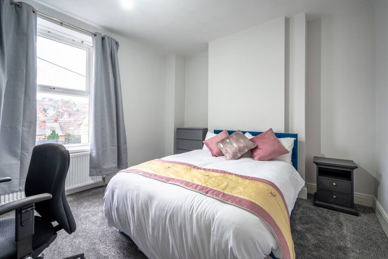 A bedroom with a bed, a chair, a nightstand, and a window with curtains.
