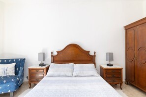 Un dormitorio con una cama de madera, dos mesitas de noche con lámparas, un armario y una silla azul estampada.