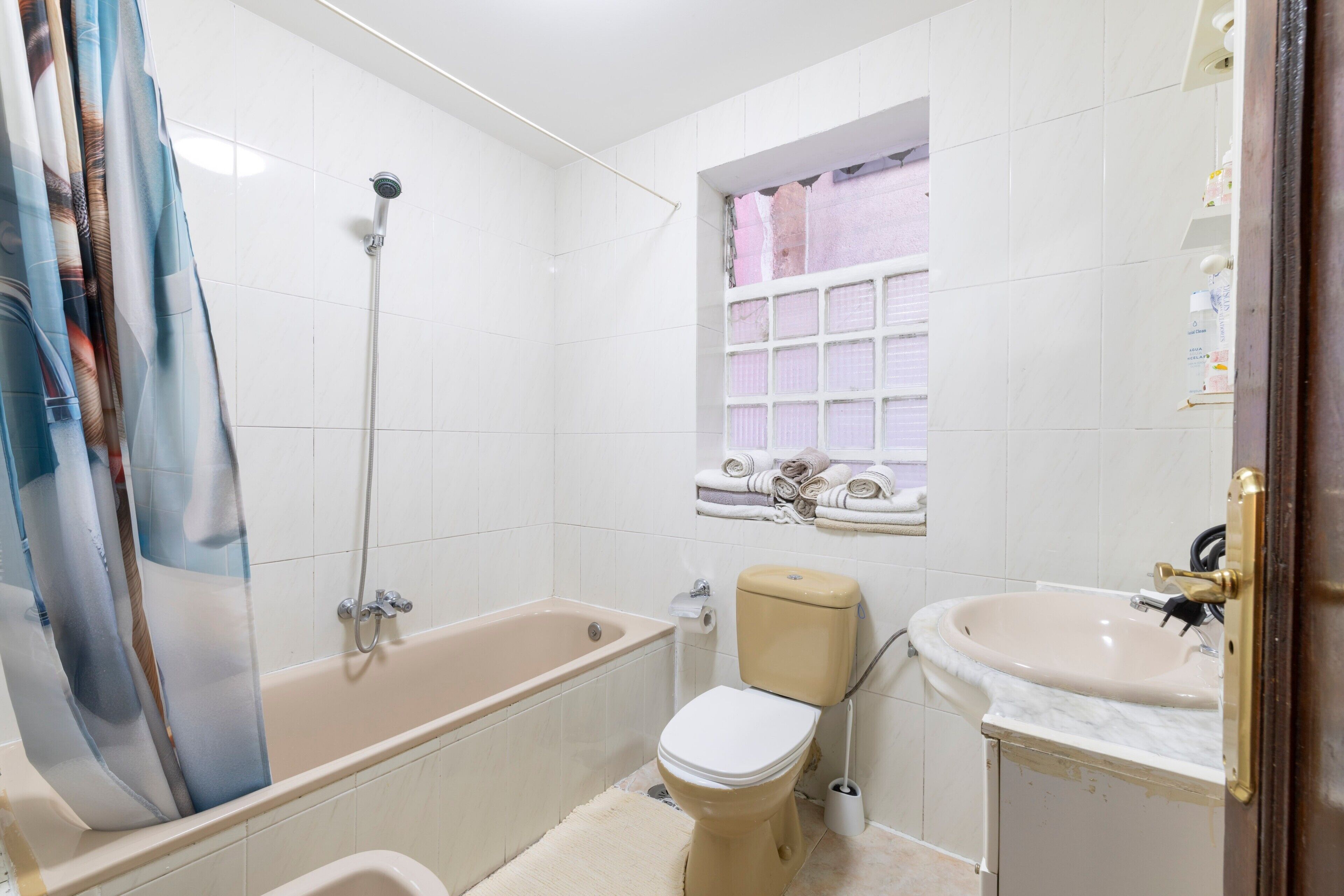 Een badkamer met een bad, toilet, wastafel en een raam met een handdoekhouder.