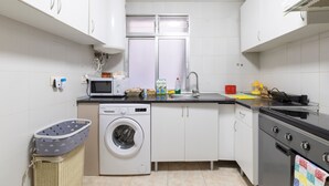 Een keuken met een wasmachine, magnetron, fornuis en kastjes.