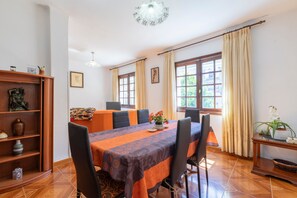 Comedor con mesa dispuesta para cuatro, una estantería y una ventana con cortinas.
