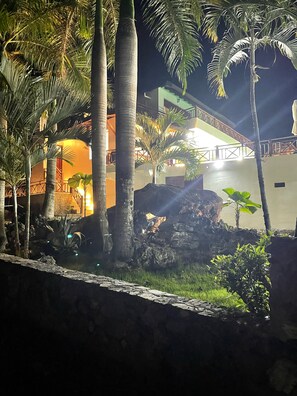 A nighttime view of a building with a stone wall, palm trees, and a well-lit entrance. - A Touch of Paradise: Villa Bahia Rincon (Samaná)