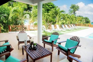 A covered outdoor seating area with lounge chairs and tables, overlooking a swimming pool and lush greenery. - A Touch of Paradise: Villa Bahia Rincon (Samaná)