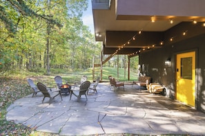 Eine Terrasse im Freien mit Adirondack-Stühlen, einer Feuerstelle und einem überdachten Bereich mit Lichterketten.