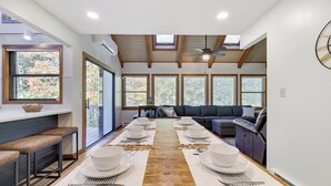 Un comedor moderno con una larga mesa dispuesta para una comida, una barra con taburetes y un área de estar acogedora con un sofá y sillones reclinables.