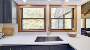 Una cocina con un lavamanos doble, marcos de ventana de madera y una encimera blanca.
