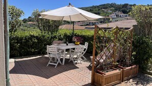 An outdoor patio with a table and chairs, a large umbrella, and wooden planters. - Malea by ColombiElbaVacanze (Capoliveri)