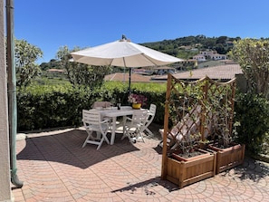 Eine Terrasse im Freien mit Tisch, Stühlen, einem großen Sonnenschirm und Holzpflanzgefäßen.