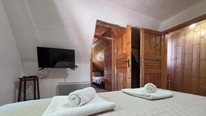 Habitación con dos camas, un televisor montado en la pared, puertas de madera y una cama con una toalla enrollada.