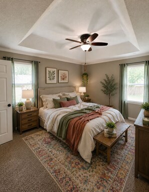 A bedroom with a bed, bedside tables, a ceiling fan, a window with curtains, and a hanging plant.