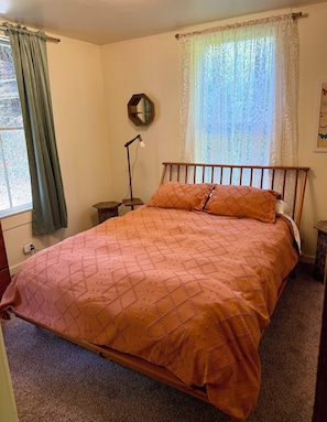Une chambre à coucher comprenant un lit, une table de chevet, une lampe, une fenêtre avec des rideaux et un miroir fixé au mur.