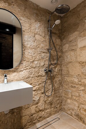A bathroom with a stone wall, a white sink, and a shower with a handheld showerhead.