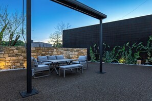 An outdoor patio with a stone wall, a metal pergola, and a seating area with cushions.