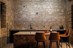 A kitchen with a stone wall, a sink, a countertop, two chairs, and a fruit bowl.