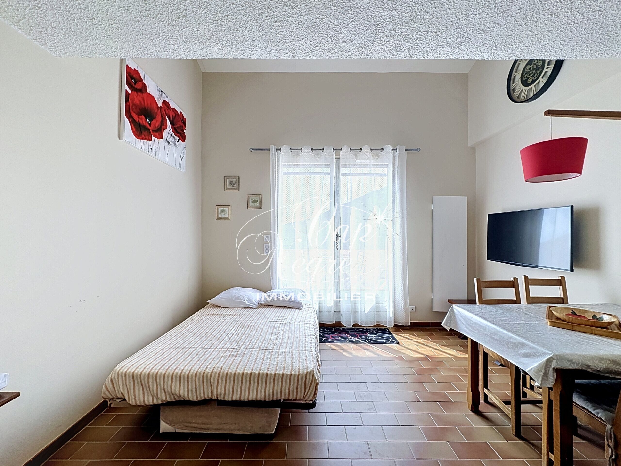 A bedroom with a bed, a TV, a dining table, and a window with curtains.