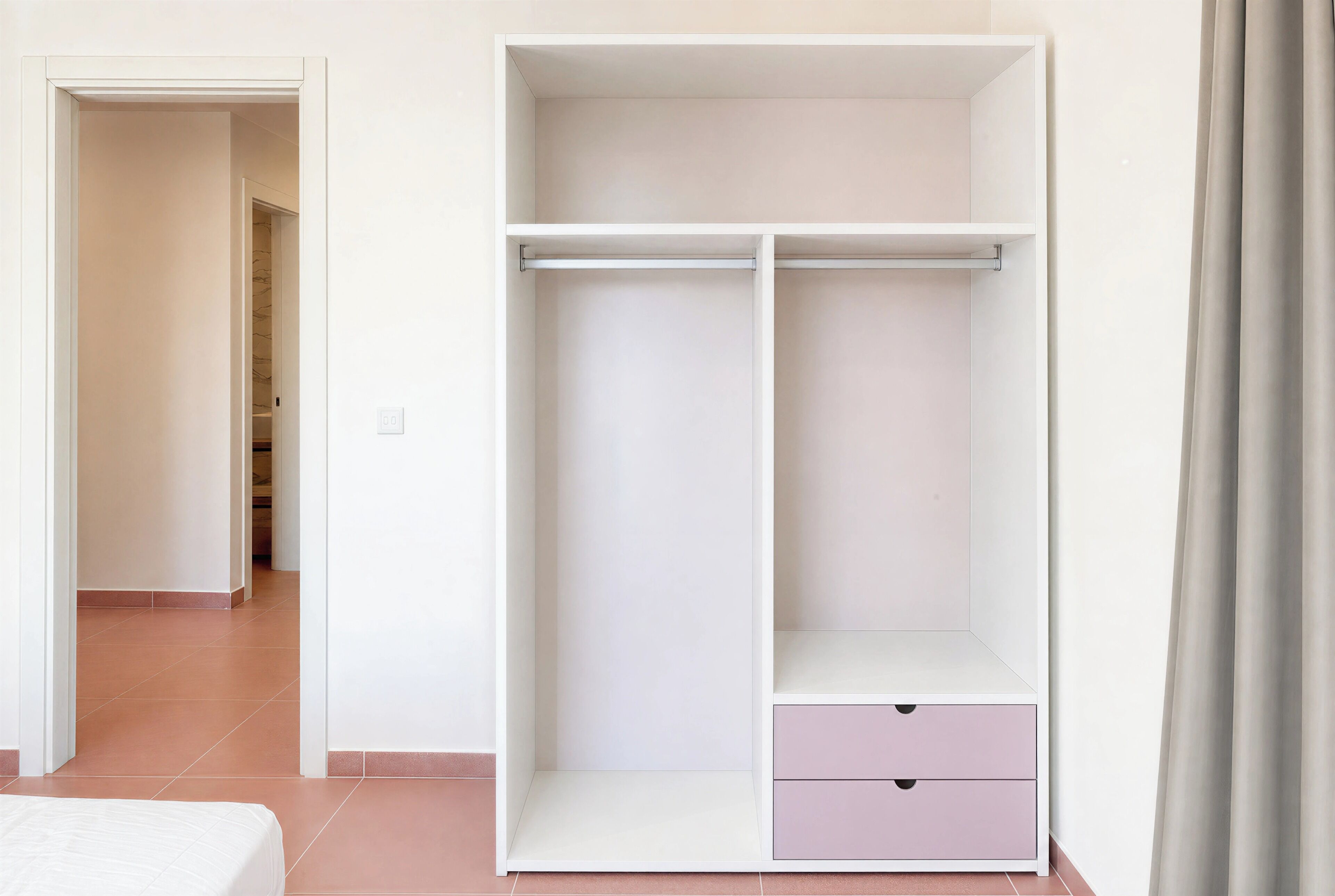 Una habitación con una cama, un armario blanco con un cajón rosa, y un pasillo que conduce a otra habitación.