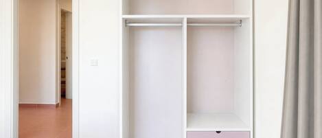 Ein Zimmer mit einem Bett, einem weißen Kleiderschrank mit einer rosafarbenen Schublade und einem Flur, der in ein weiteres Zimmer führt.