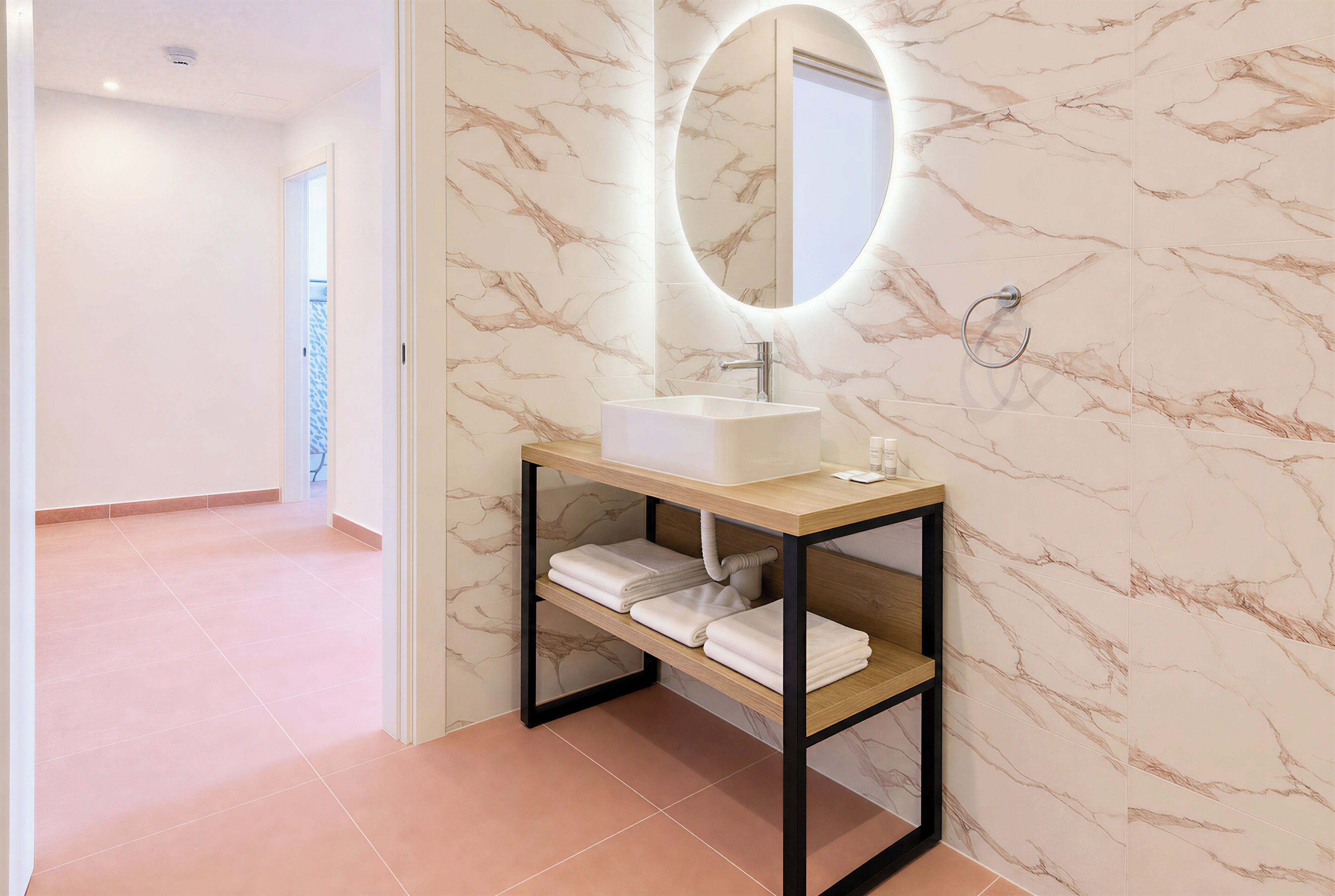 Une salle de bain avec un mur en marbre, un lavabo blanc, un miroir et un porte-serviettes.