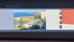 A view from a window overlooking a coastal area with buildings, a beach, and a clear sky. - Flamingo Apartments in Vegas Resort, Malta (San Ġiljan)