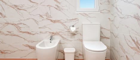 A bathroom with a bidet, toilet, and a small trash bin.
