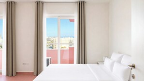 A hotel room with a bed, curtains, a nightstand, and a view of the city. - Flamingo Apartments in Vegas Resort, Malta (San Ġiljan)