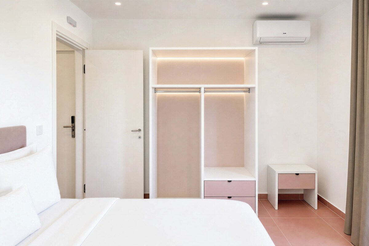 A hotel room with a bed, a wardrobe with illuminated shelves, a bedside table, and an air conditioning unit.