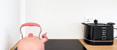 A pink kettle on a black induction cooktop, a black toaster oven, and a white wall with a power outlet.