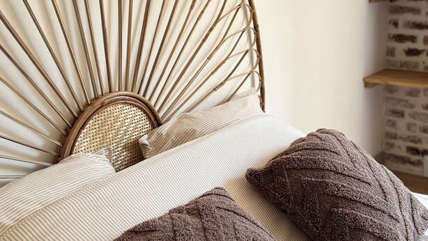 A bed with a woven headboard, striped bedding, and two brown pillows. - Cosy apartment on the banks of the Nivernais Canal (Saint-Léger-des-Vignes)