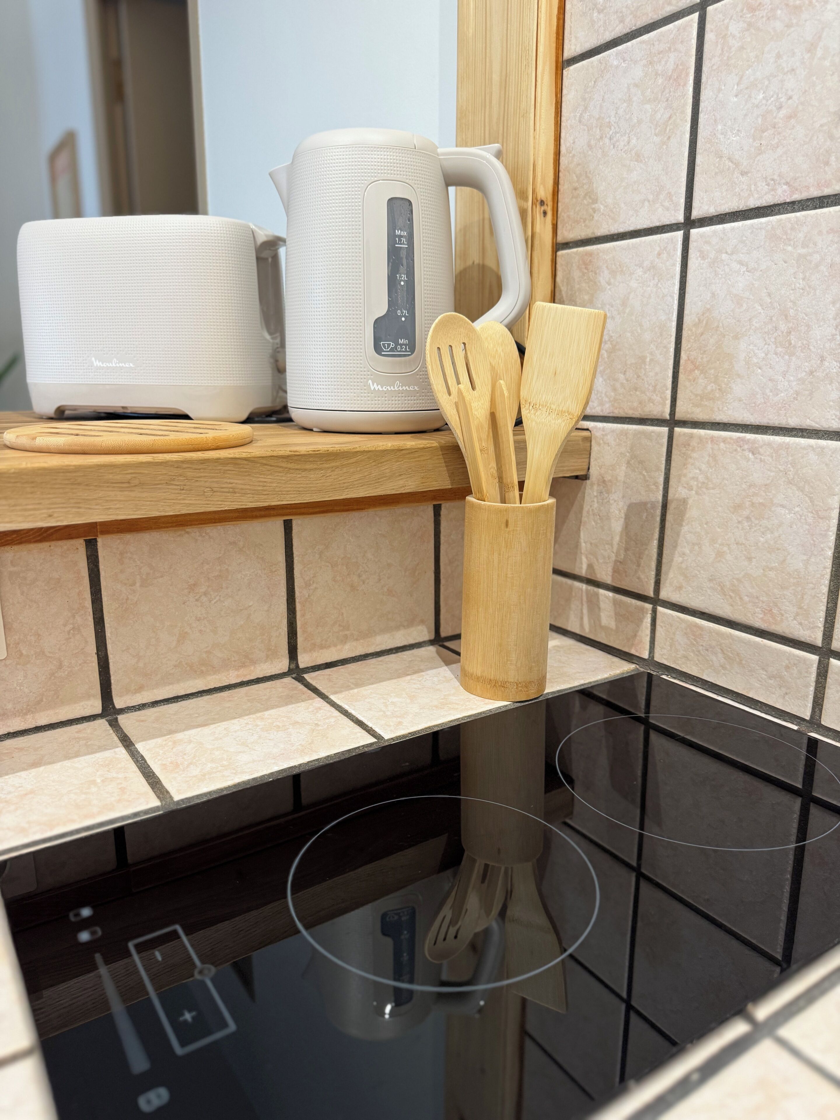Eine Küche mit einem weißen Wasserkocher, einem Holzer Schneidebrett und Holzkocherutensilien in einer Halterung.