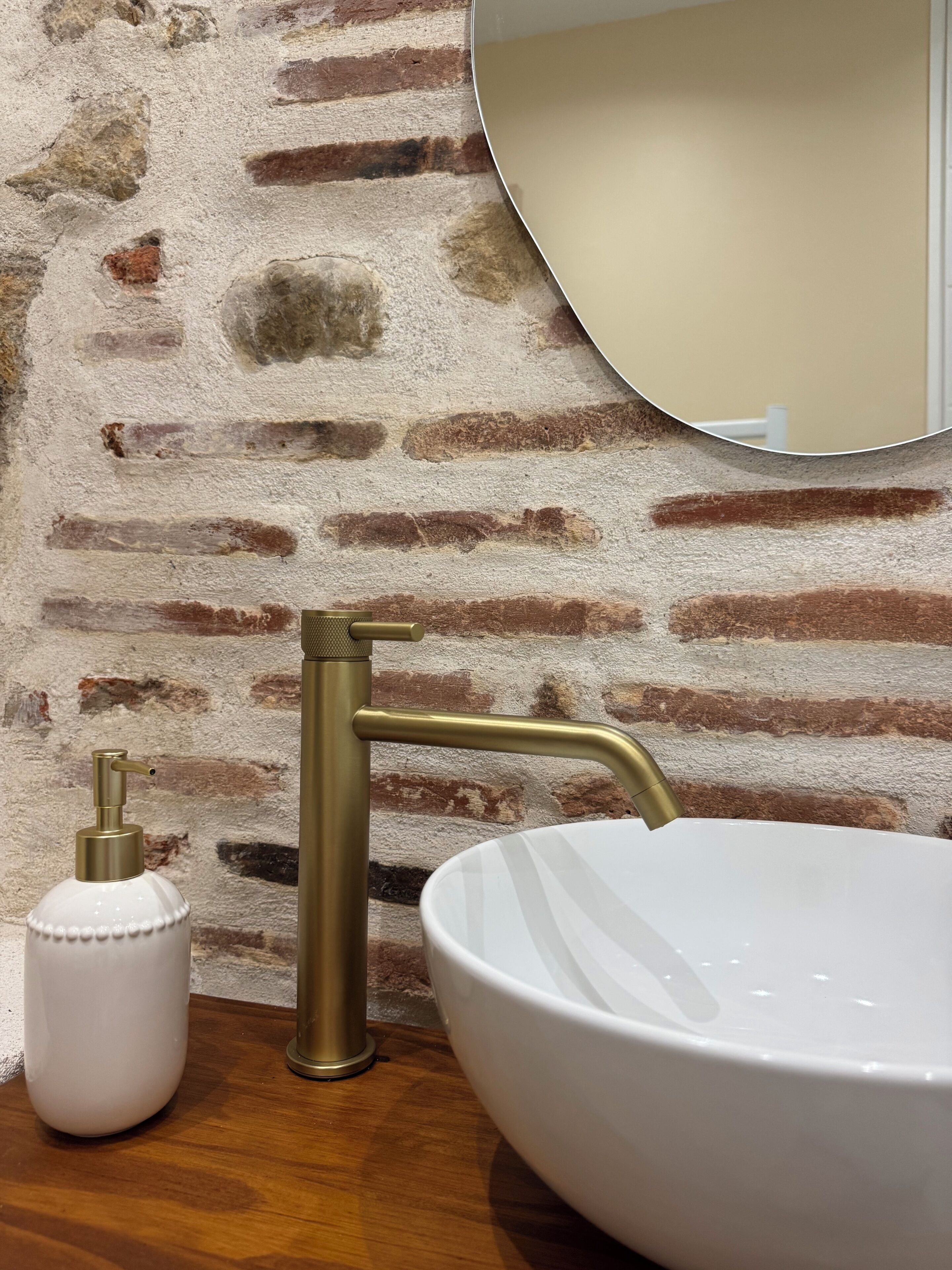 A bathroom with a white sink, brass faucet, and a soap dispenser.